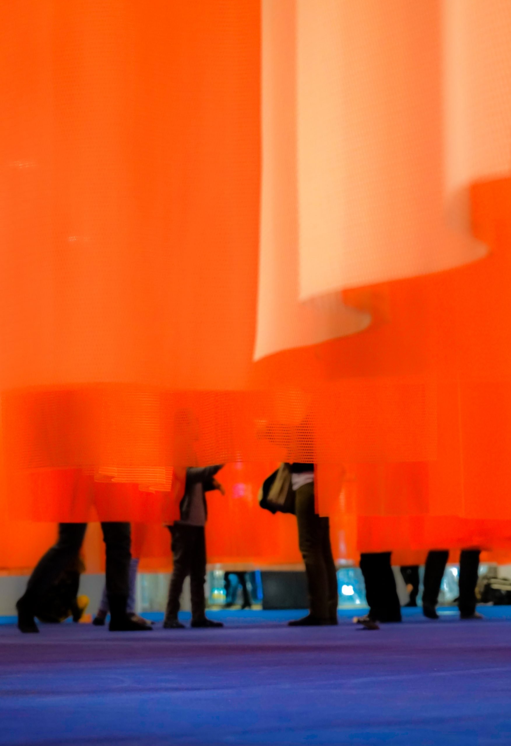 Des rideaux de couleurs chaudes, sous lesquels des pieds apparaissent.