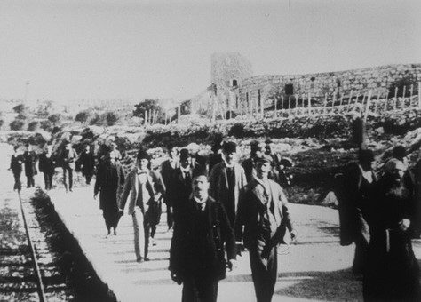 Des hommes marchant sur un quai et regardant l'objectif de l'appareil que l'on devine posé sur un train en marche