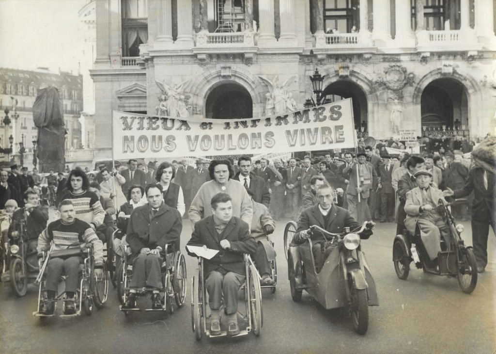 Handicapés manifestant derrière une banderolle : Vieux et infirmes, nous voulons vivre