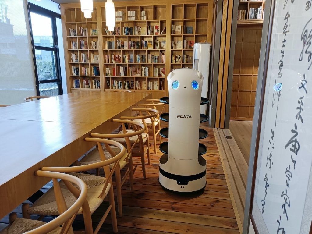 Un robot devant une table et une étagère de livres.