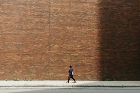 Une femme marche devant un immense mur en brique