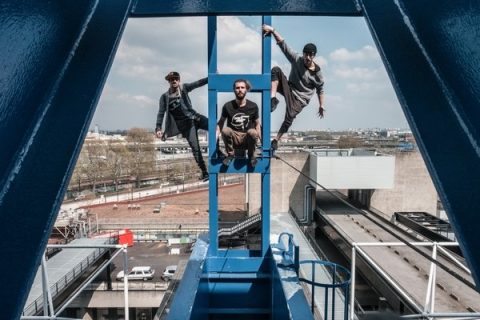 Trois membres du groupe French Freerun Family posant sur une structure structure métallique dominant une ville