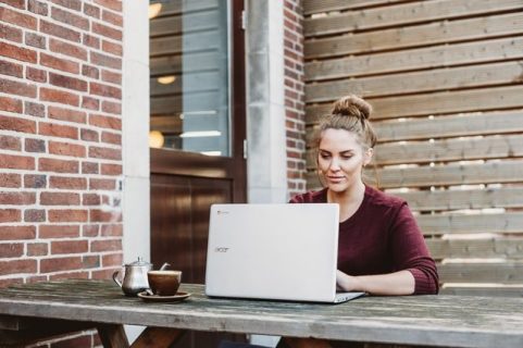 Une femme devant son ordinateur, en extérieur, sur une table de jardin