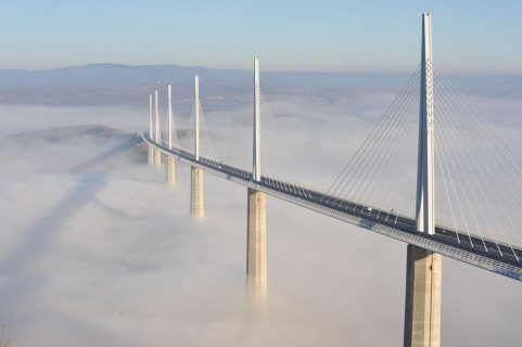 Un pont émarge des nuages. Ses piliers blancs et ses haubants clairs soutiennent un ruban de bitume.