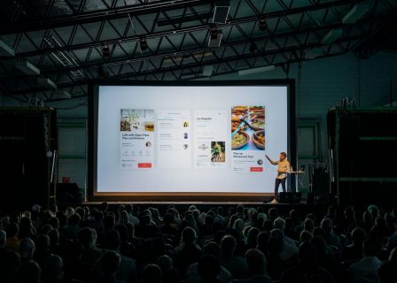 Une personne présente une page web sur un écran de cinéma devant une salle pleine